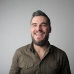 Portrait of a bearded man smiling joyfully in a casual studio setting.
