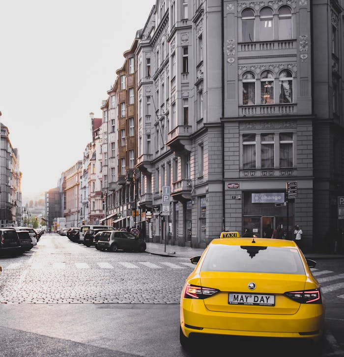zipwp-image-1324990 Yellow taxi in a classic Prague street with historical architecture under daylight.