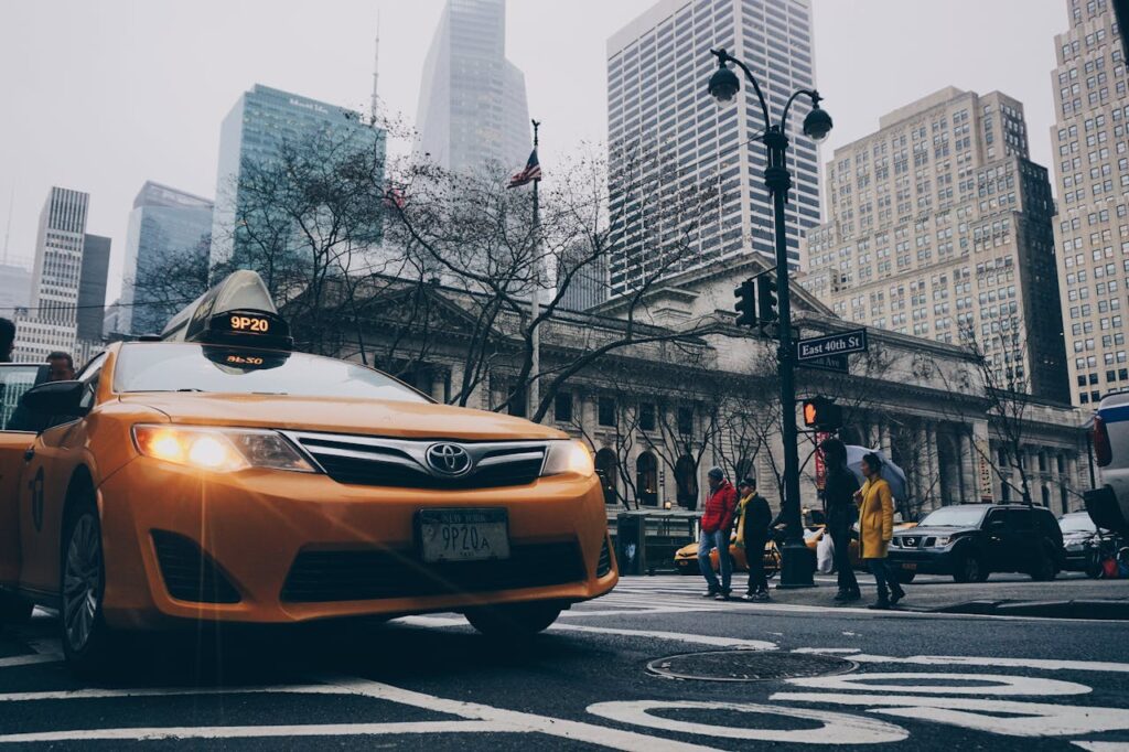 zipwp-image-314374 A bustling New York City street intersection featuring a yellow taxi and pedestrians with skyscrapers in the background.